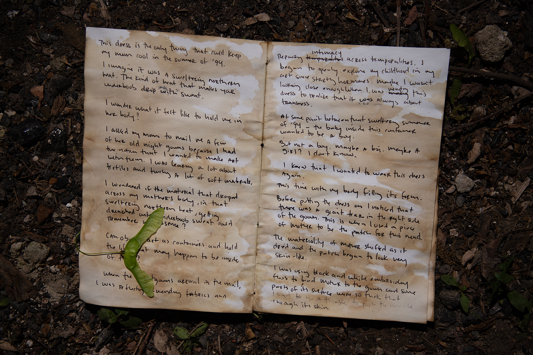 A hand-written diary laying on dirt and is opened directly to the middle of the diary. 