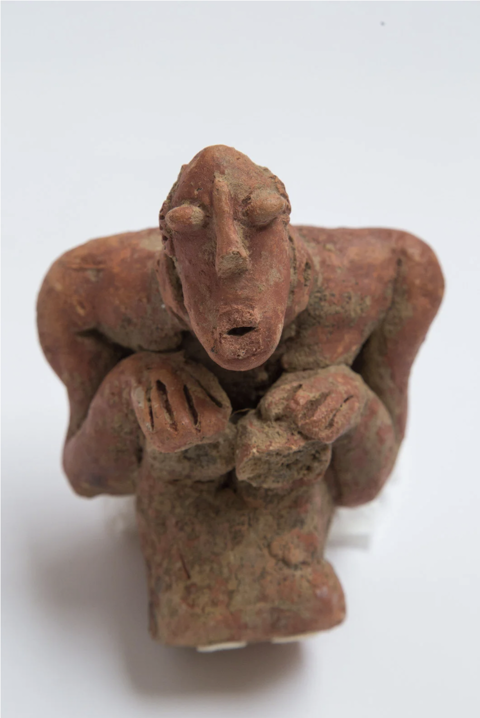 Image of 15th century Malian Djenné terracotta in crouching position and expressive face; hands are placed on the knees and the eyes and mouth are round and prominent.